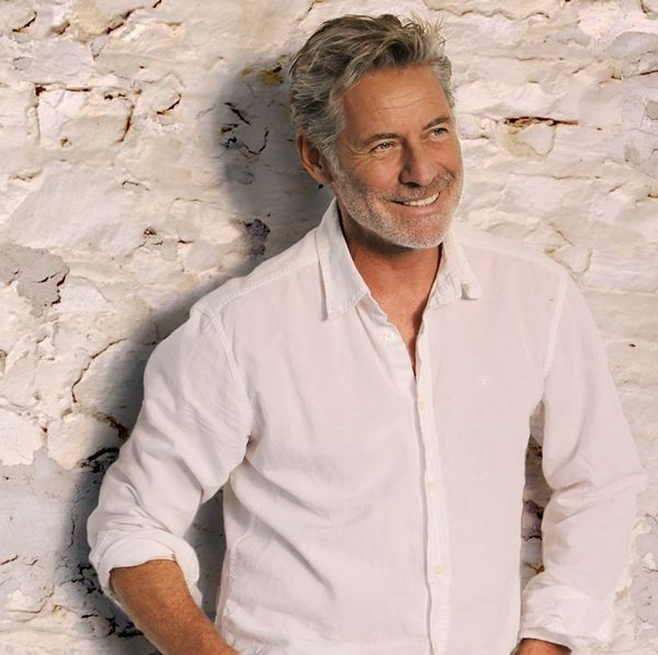 Déclic au Fancy Club homme chemise blanche souriant sur un mur en brique